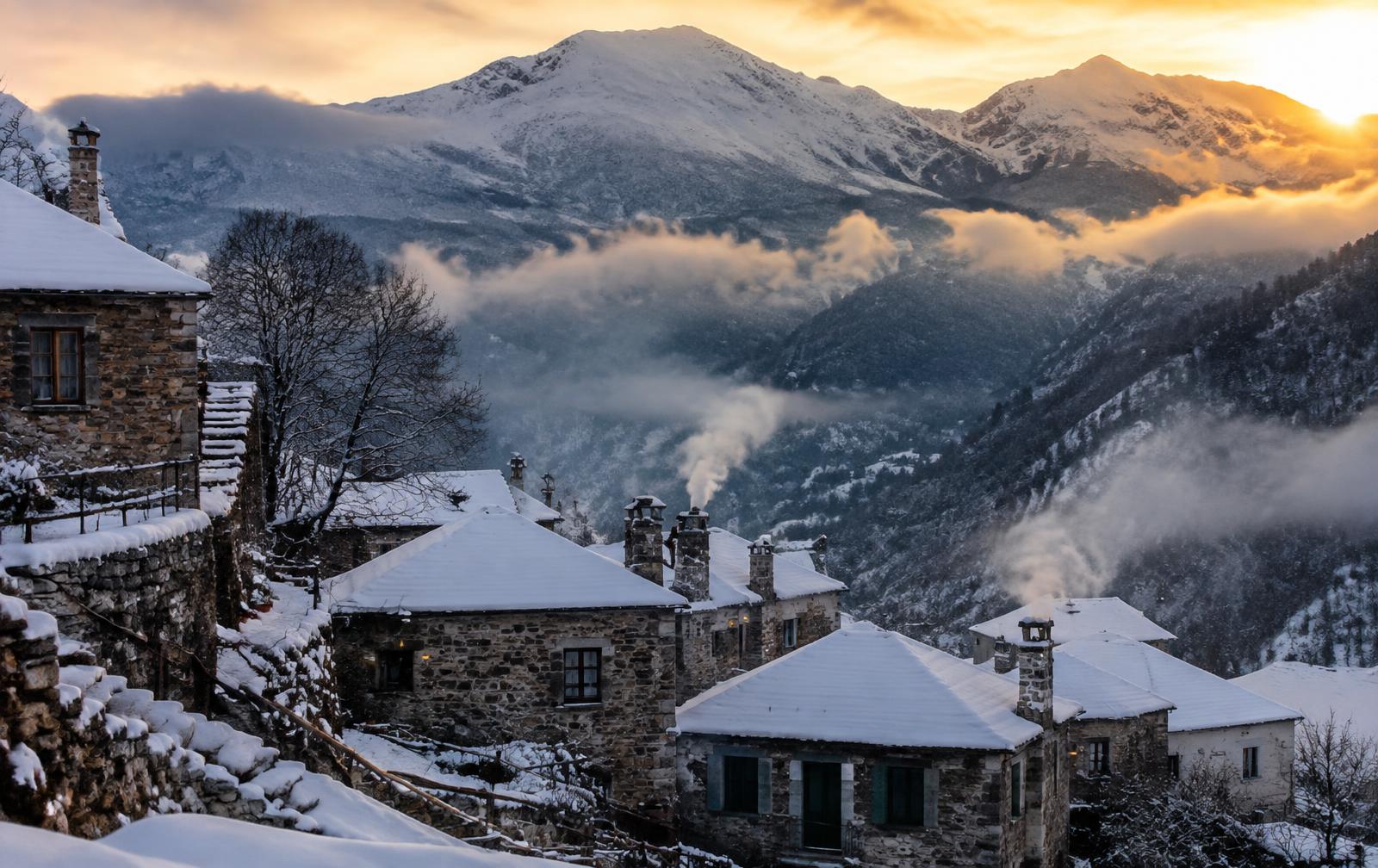 Snow-covered stone village in Zagori with mountains at sunset